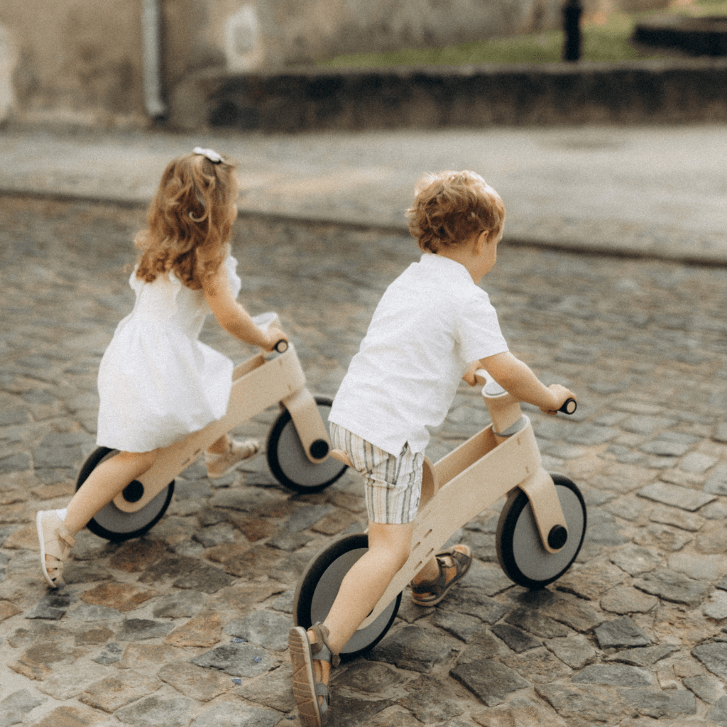 dziecko pcha rowerek balance bike chodząc po parku z pomocą rodzica